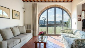 A living room with a large arched window, a sofa, a coffee table, and a patterned armchair. - Beautiful  villa for 12 guests with private pool, WIFI, TV, terrace, pets allowed and panoramic ... (Scandicci)