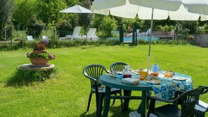 Une terrasse avec une table dressée pour un repas, entourée de chaises, et un grand parasol offrant de l’ombre.