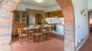 Une cuisine avec une arche en briques, des armoires en bois, une table à manger avec des chaises et un sol carrelé.