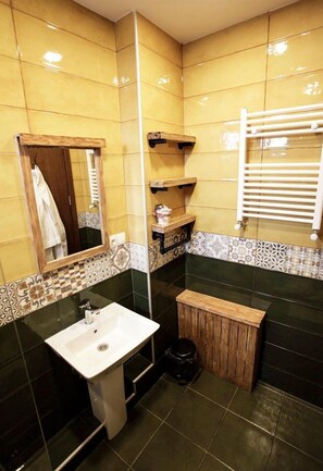 A bathroom with a white sink, a mirror, a wooden bench, and a towel rack.