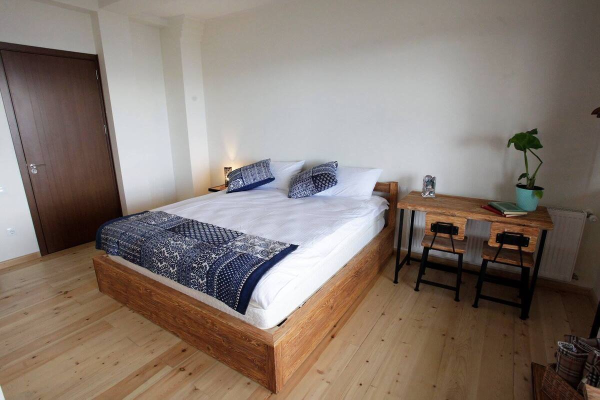 A bedroom with a wooden bed, a small wooden desk, and a potted plant.