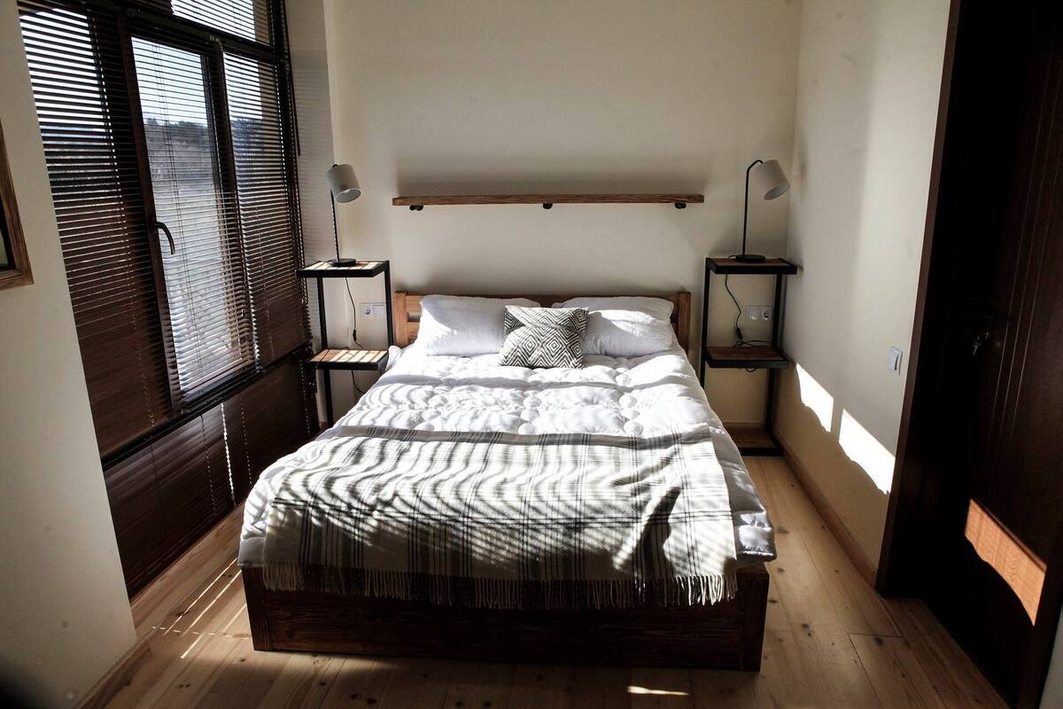 A small, cozy bedroom with a bed, bedside tables, and a window with blinds.