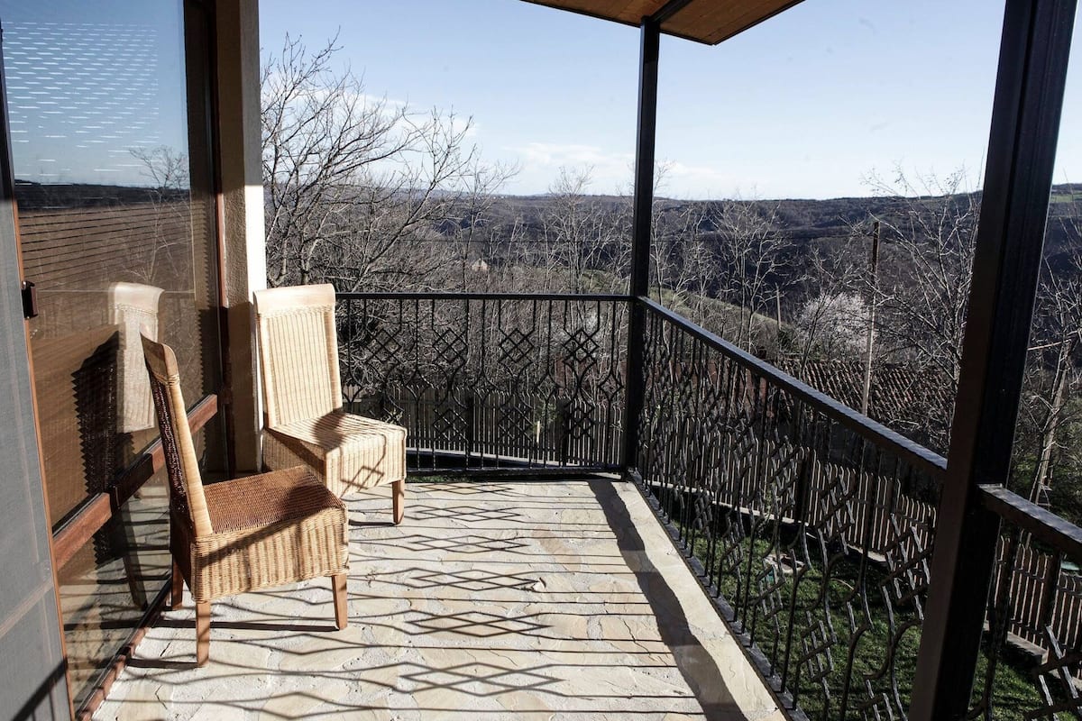 A balcony with a wicker chair and a view of a mountainous landscape.
