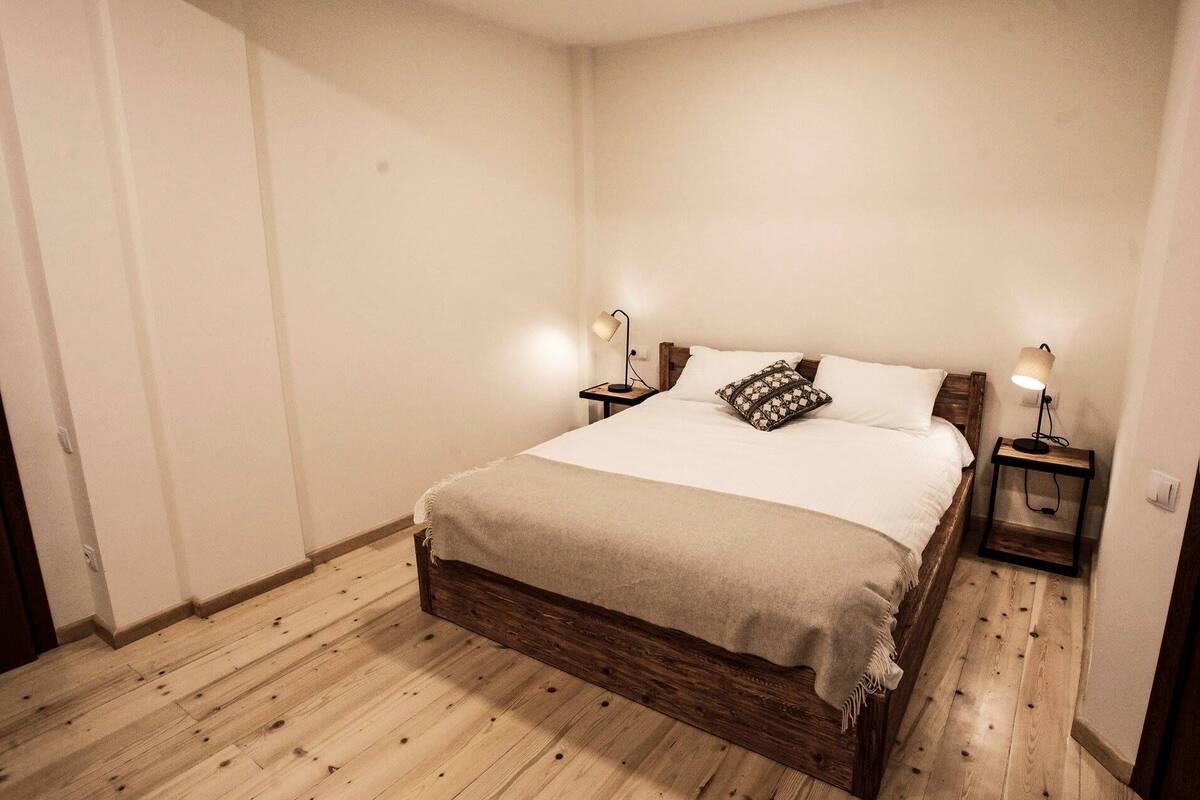 A bedroom with a wooden bed, two bedside tables with lamps, and a patterned pillow.
