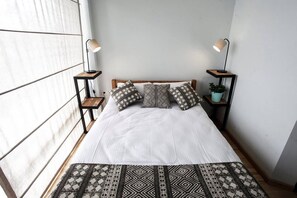 Een net opgemaakt bed met gestreepte kussens, twee bedlampen en een kleine plant op een nachtkastje.