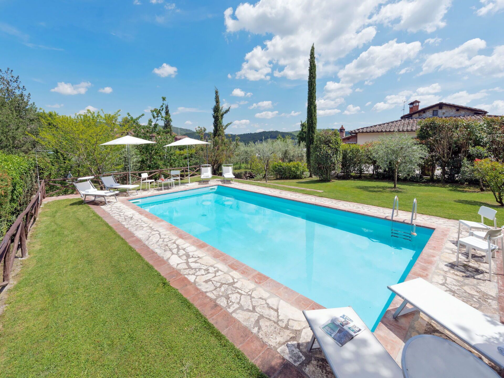 Una piscina rectangular con borde de piedra, rodeada por un césped cuidado y árboles.
