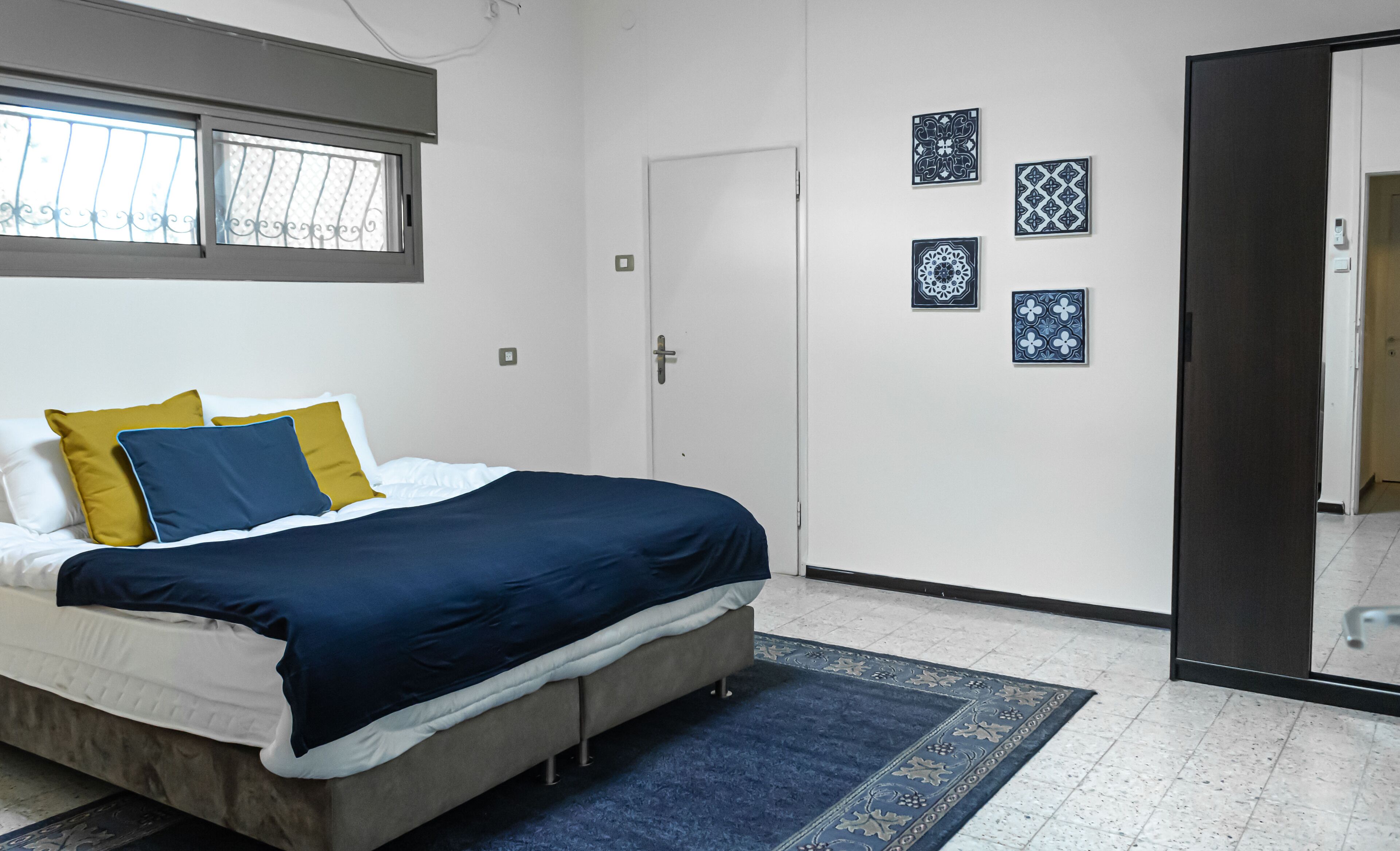 Een slaapkamer met een bed, een deur en vier decoratieve tegels aan de muur.