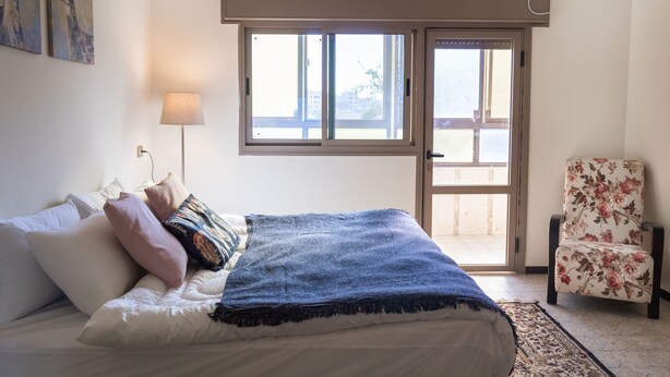 A bedroom with a bed, pillows, a lamp, a chair, and a window with a view. - Old City Stylish 4BR by Ahlan Hospitality (Nazareth)