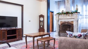 A living room with a flat-screen TV, wooden furniture, a fireplace, and a floral-patterned cushion. - Old City Stylish 4BR by Ahlan Hospitality (Nazareth)