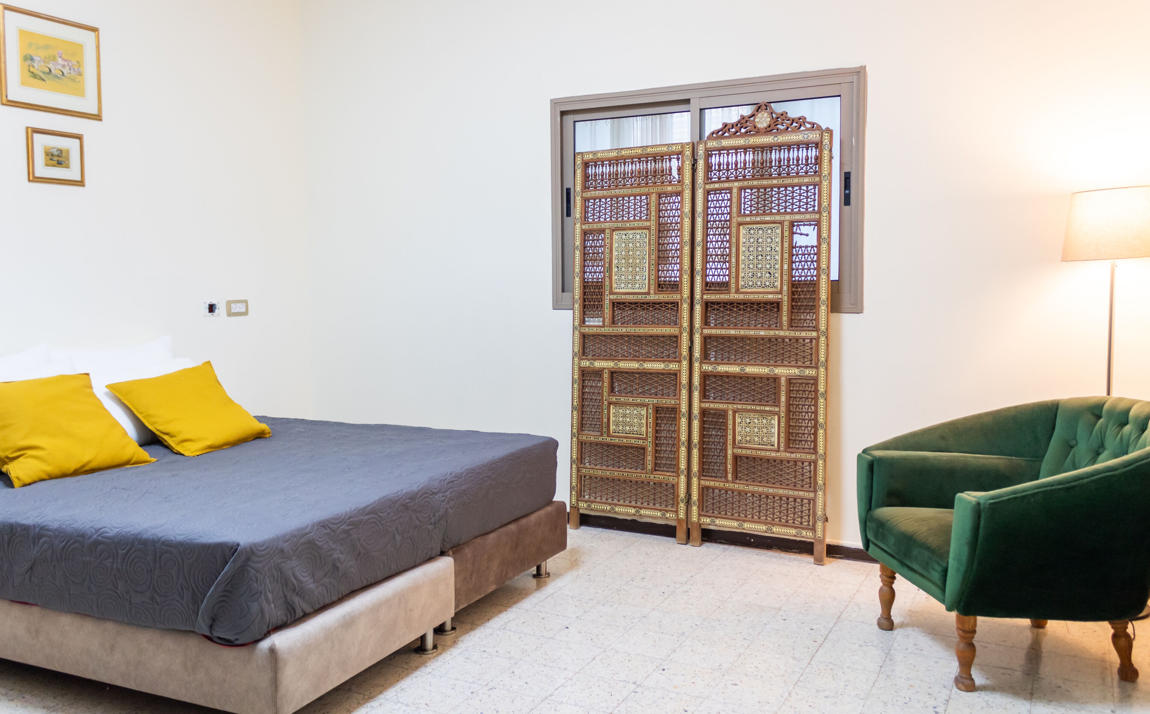 A bedroom with a bed, a green armchair, a decorative wooden door, and a lamp.