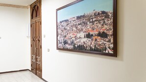 A hallway with a large framed cityscape painting on the wall and a wooden door. - Old City Stylish 4BR by Ahlan Hospitality (Nazareth)