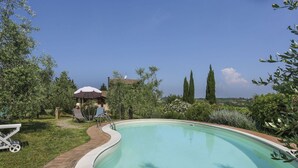 A swimming pool with a curved edge, surrounded by a brick pathway and greenery.
