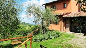A rustic house with a stone foundation and a tiled roof, surrounded by lush greenery and a gravel path.