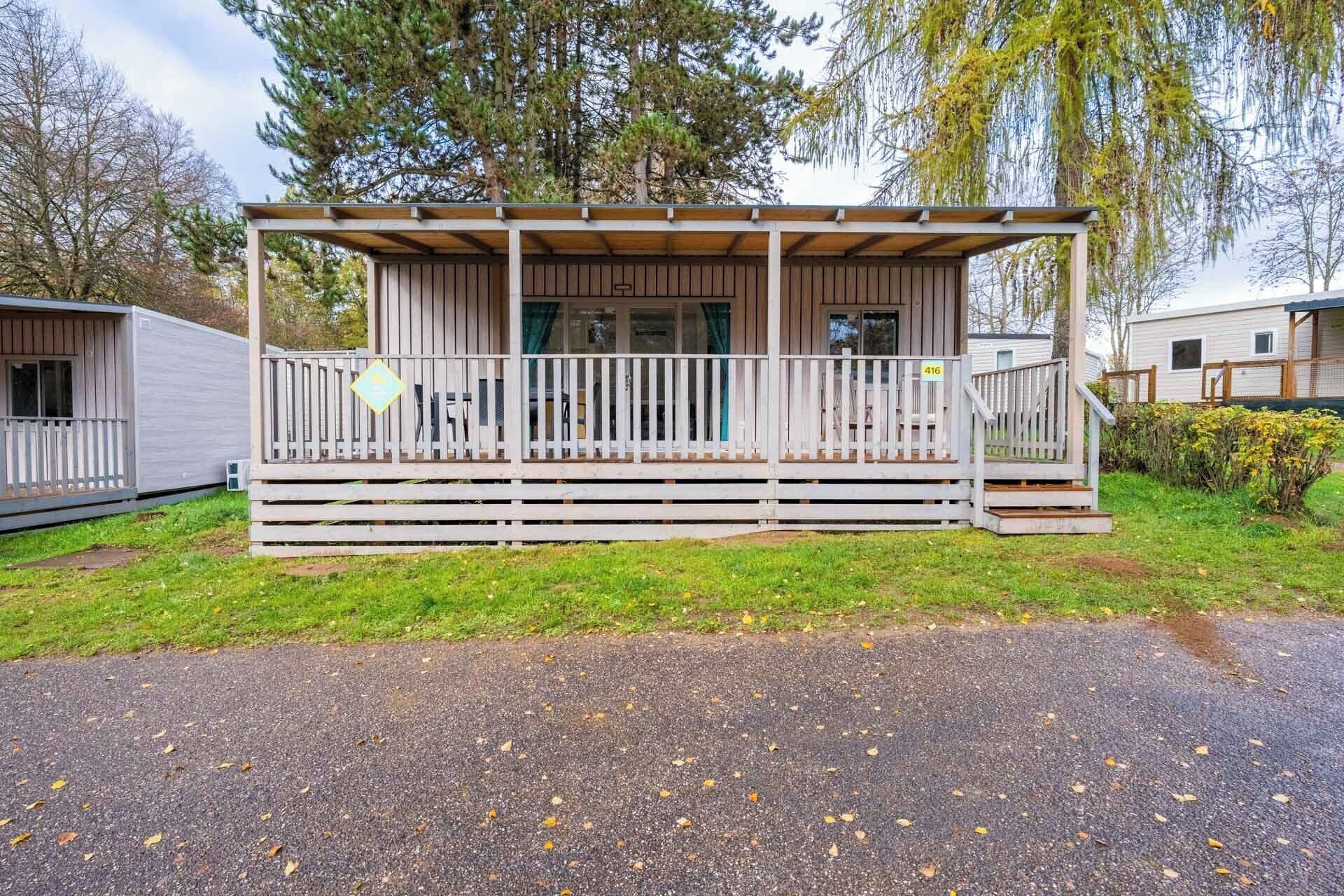 A mobile home with a porch, a fenced deck, and a number sign indicating its unit.