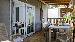 A covered outdoor area with a table, chairs, and a sliding glass door leading to an interior space. - Hu Birkelt Village (Larochette)