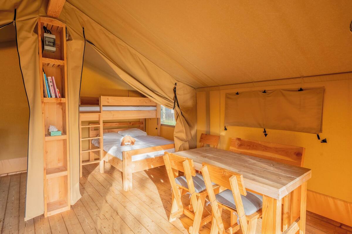 A cozy tented room with a bunk bed, a wooden table with chairs, a bookshelf, and a window.