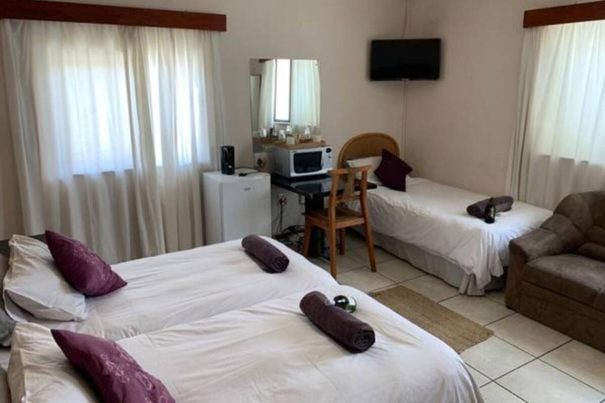 Habitación de hotel con dos camas, un escritorio con microondas, televisor y sofá.
