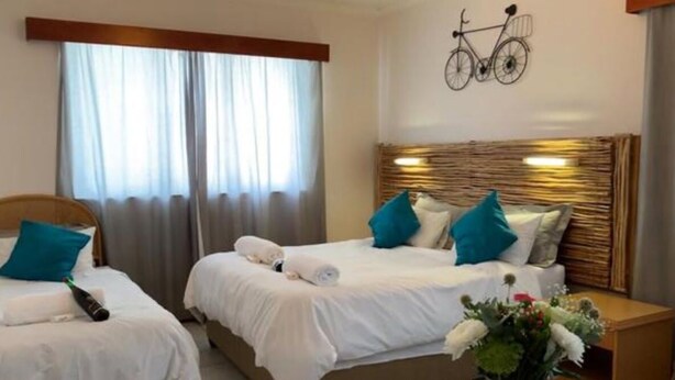 A hotel room with two beds, a bicycle wall decoration, and a vase with flowers. - The Lodge Strand (Cape Town)