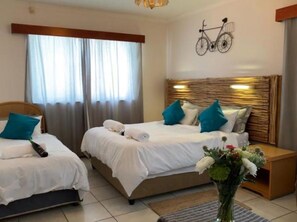 A hotel room with two beds, a bicycle wall decoration, and a vase with flowers. - The Lodge Strand (Cape Town)