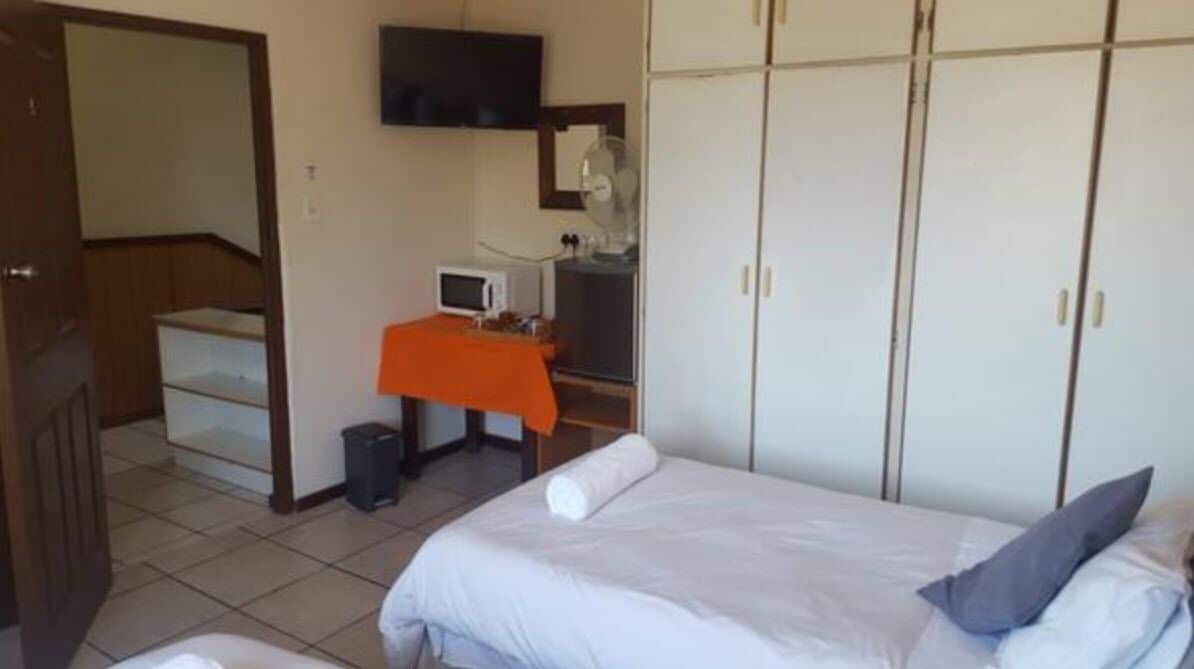 A bedroom with a bed, a desk with a chair, a television mounted on the wall, and a wardrobe.