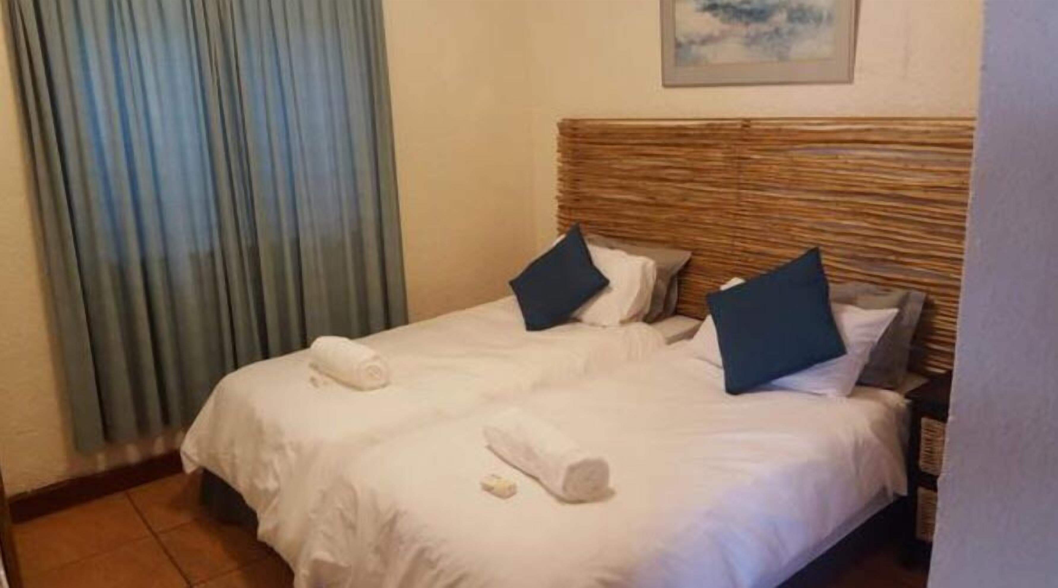 A double bed with white bedding and two pillows, a rolled towel, and a small item on the bed.
