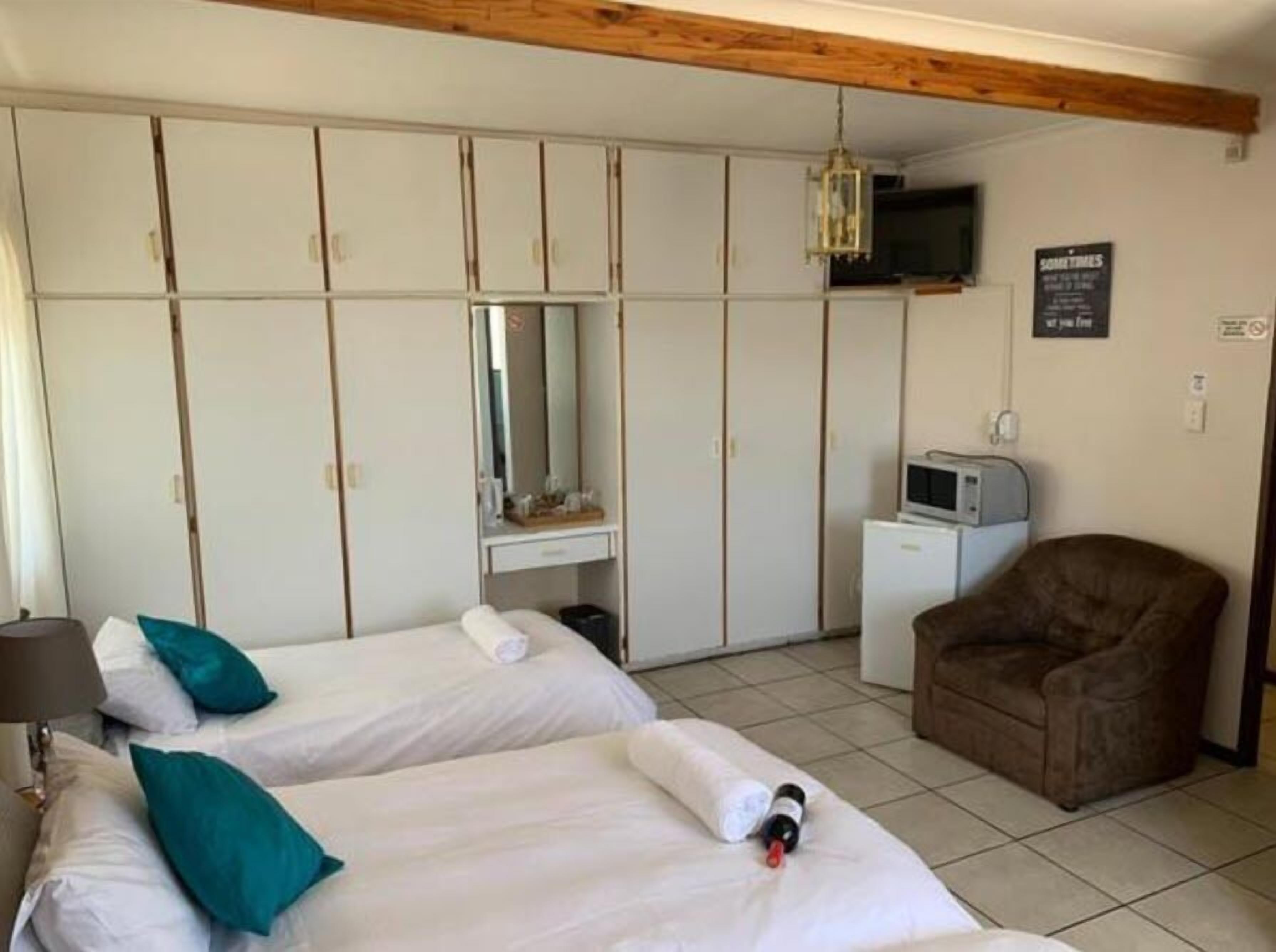 Een hotelkamer met twee bedden, een bruine fauteuil, een televisie en een minibar.