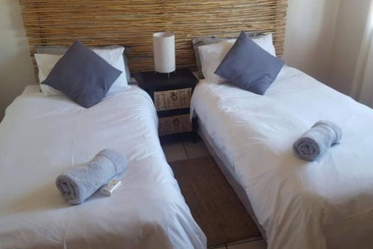 Habitación doble con dos camas, cada una con una toalla enrollada y una almohada.
