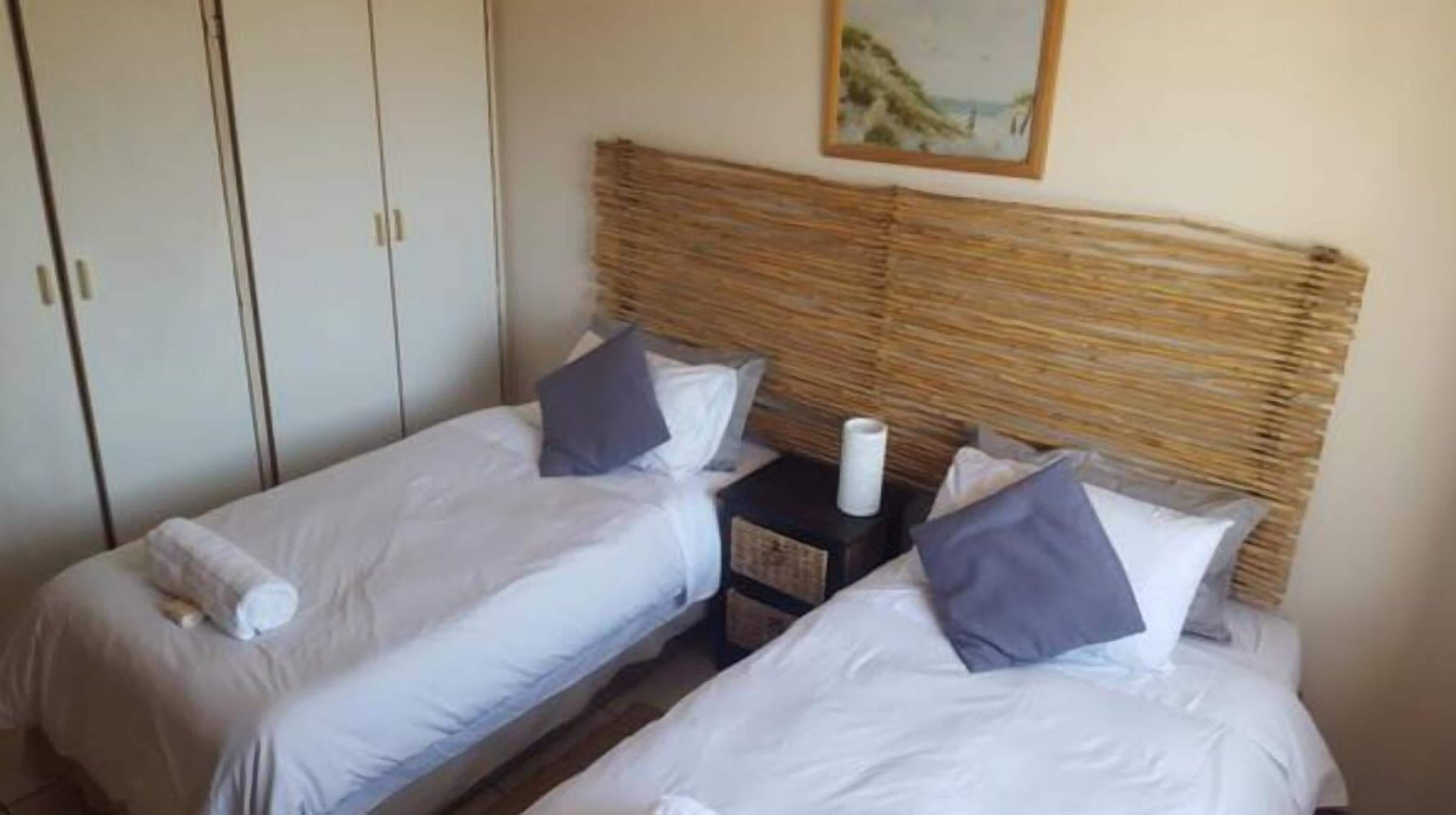 A bedroom with two single beds, a nightstand with a lamp, and a painting on the wall.