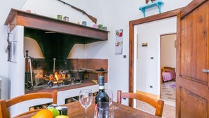 A rustic dining area with a wooden table, chairs, a bottle of wine, and a fruit bowl. A fireplace is visible in the background. - Wonderful private villa for 11 guests with WIFI, TV, balcony and pets allowed (Sinalunga)