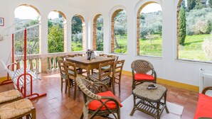 A dining area with a wooden table and wicker chairs, large arched windows with a view of greenery, and a red exercise bike. - Wonderful private villa for 11 guests with WIFI, TV, balcony and pets allowed (Sinalunga)
