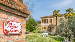 A sign reading "Poderi Cosina" on a brick wall, with a garden and a stone building in the background. - Wonderful private villa for 11 guests with WIFI, TV, balcony and pets allowed (Sinalunga)