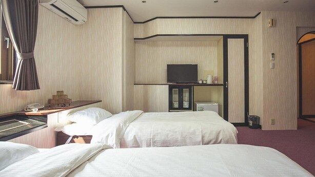 Habitación de hotel con dos camas, un escritorio con teléfono, un equipo de aire acondicionado y un televisor sobre un mueble.