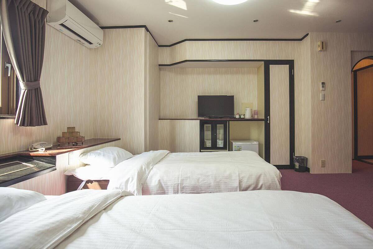 Une chambre d’hôtel avec deux lits, un bureau avec un téléphone, un appareil de climatisation et un téléviseur posé sur un meuble.