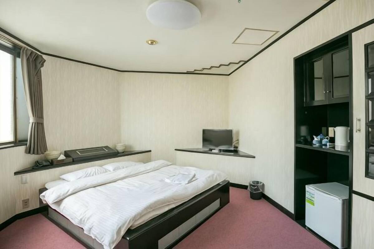 Une chambre d’hôtel équipée d’un lit, d’une télévision, d’un bureau, d’une armoire et d’une fenêtre avec des rideaux.