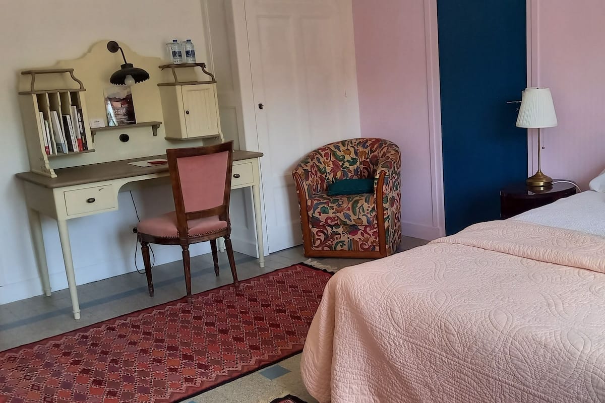 A bedroom with a bed, a desk with a chair, a nightstand, and a patterned rug.