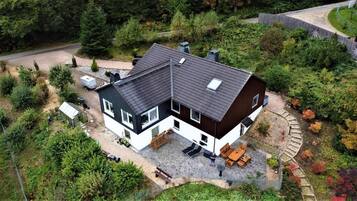 A two-story house with a sloped roof, a patio with outdoor furniture, and a garden area.