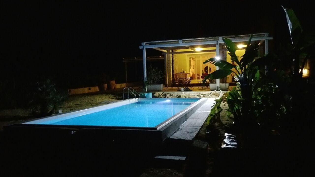En swimmingpool med en overdækket terrasse og en bygning i baggrunden.