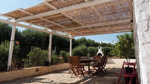 Eine Außenpatio mit Pergola, Steinböden, Holzsitzen und roten Stühlen sowie einem Tisch mit einer Laterne.