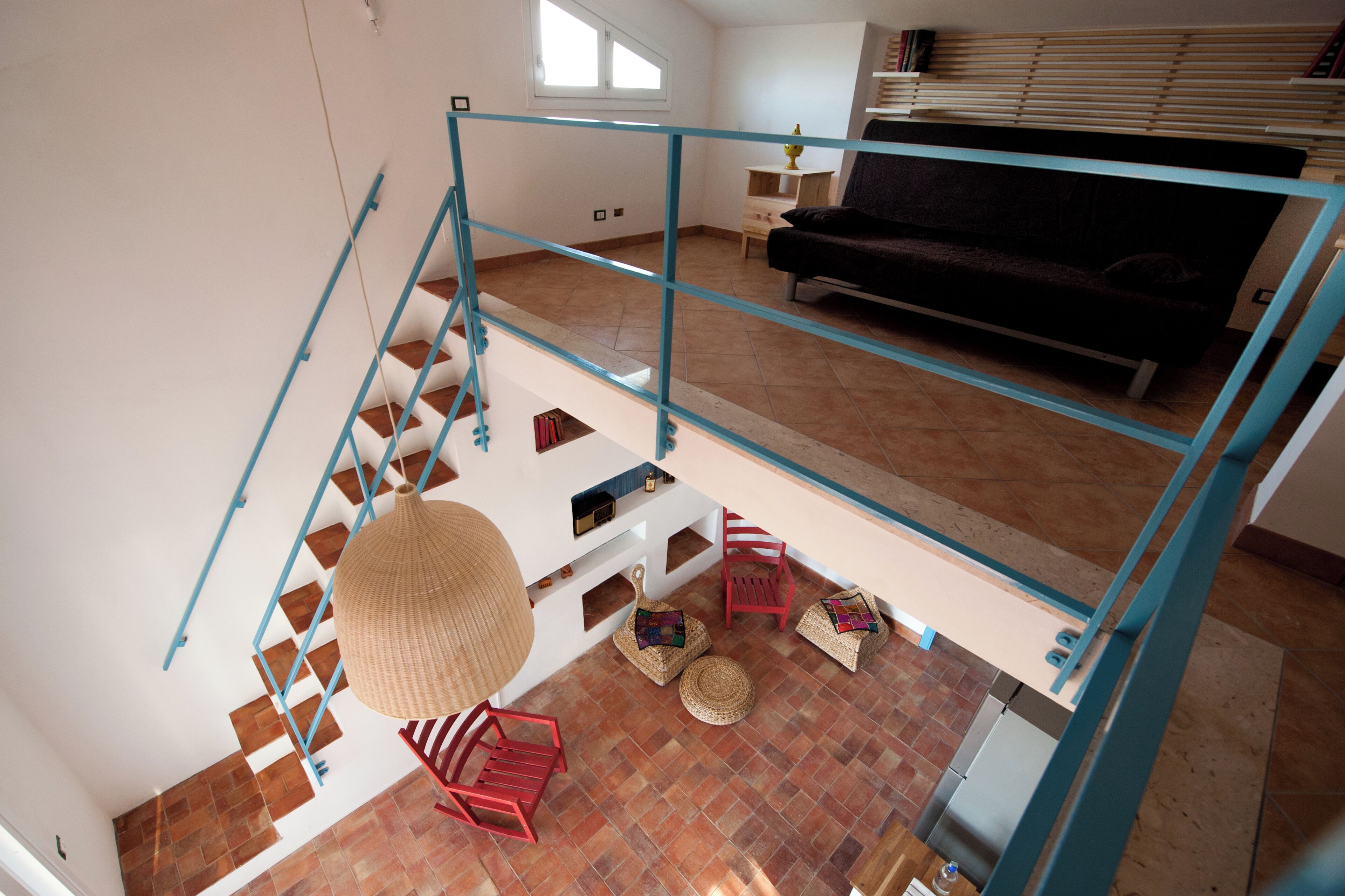 Ampla sala de estar com escada, um sofá escuro e uma mesa de jantar.