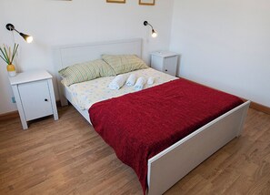 A neatly made bed with a red blanket, two bedside tables with lamps, and a small potted plant on one table. - Jabia Beach House - Villa on the Beach - Private Beach (Castelvetrano)