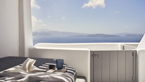 Un balcón con vista al mar y a las montañas, una mesa con un libro, una copa y una taza.