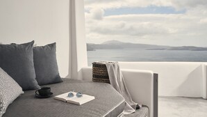 Un dormitorio con vista al mar, una cama con ropa de cama gris, una taza negra y un par de gafas de sol sobre un libro abierto.