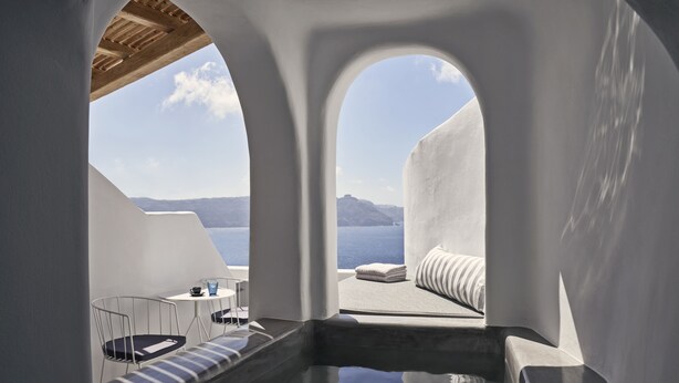 Una habitación moderna y minimalista con vistas despejadas al mar y montañas distantes. Cuenta con una zona de estar con un banco acolchado y una pequeña mesa con una taza.