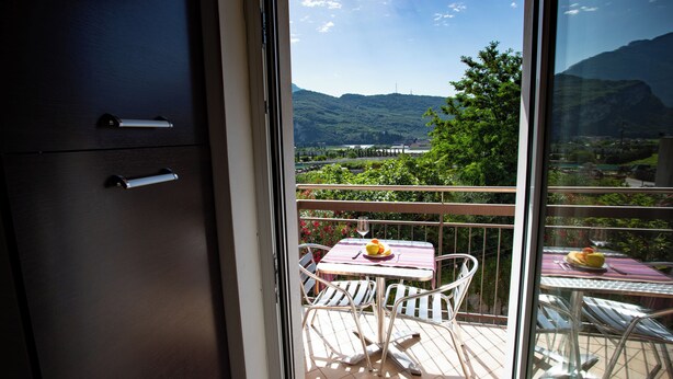 Un balcon avec une table et des chaises, une vue sur un paysage montagneux et une porte vitrée donnant sur une pièce avec un placard.