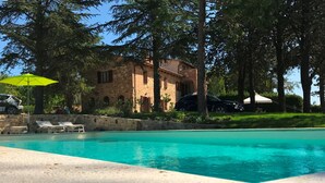 A swimming pool with lounge chairs and umbrellas, surrounded by trees and a stone building. - Welcome at Poggio Cantarello Country Home Tuscany (Chiusi)