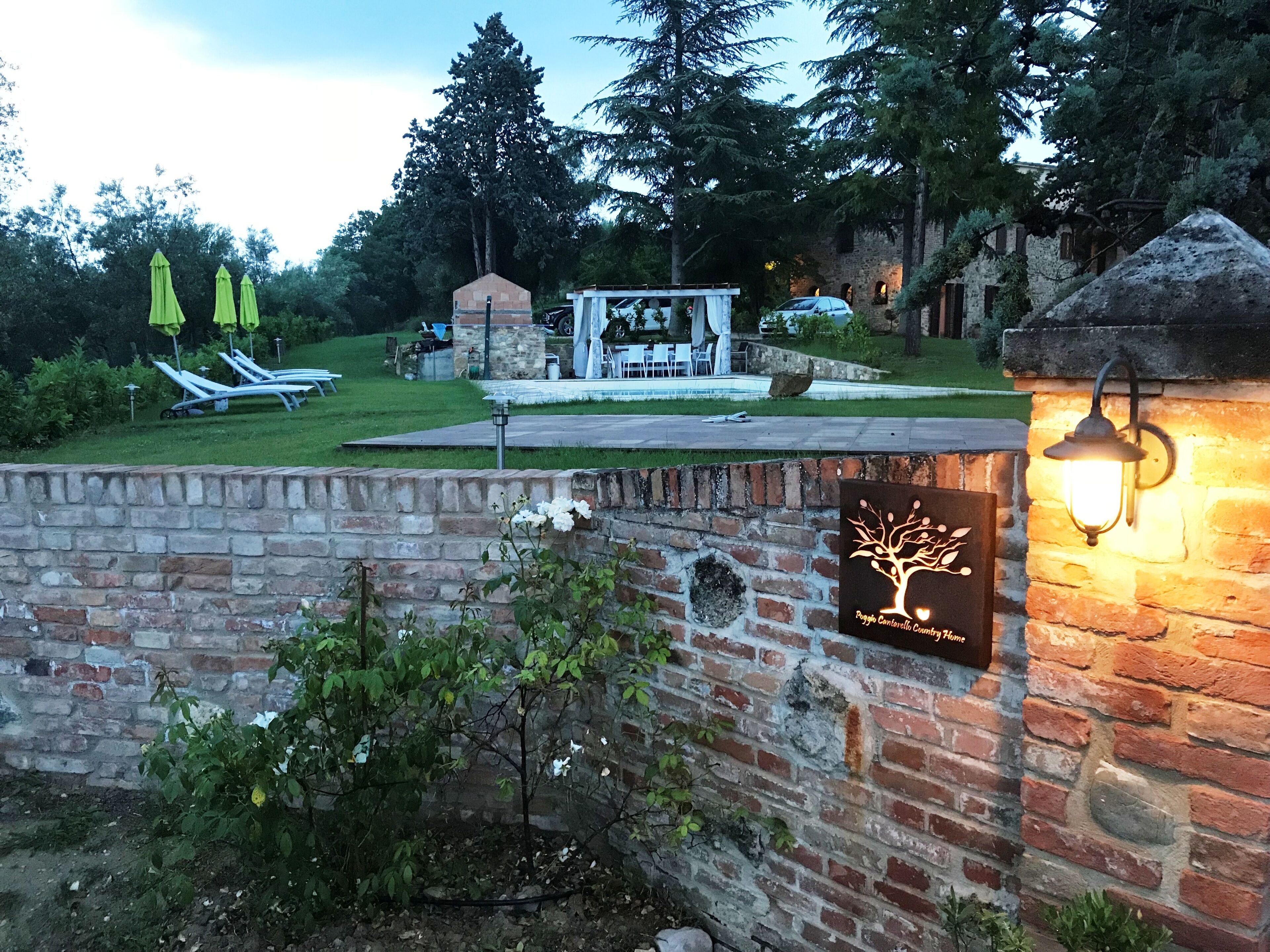 A brick wall with a sign, a stone lantern, and a garden with a gazebo and lounge chairs.