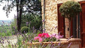 A stone building with a wooden door and a flower bed with lavender and pink flowers. - Welcome at Poggio Cantarello Country Home Tuscany (Chiusi)