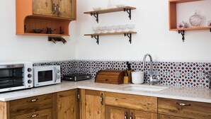 A kitchen with wooden cabinets, a microwave, a toaster, a sink, and decorative glassware on shelves. - Heart of Old city 3BR by Ahlan Hospitality (Nazareth)