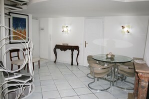 A dining area with a glass table surrounded by chairs, a wooden side table, and a white door with a brass handle. - Apartment at the Roman Forum in the Center of Rome (Rome)