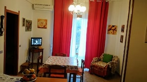Ein Essbereich mit Tisch, Stühlen, einem Fernseher und einem Fenster mit roten Vorhängen.